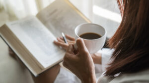 Asian,Woman,Holding,Cup,Of,Coffee,And,Reading,A,Book